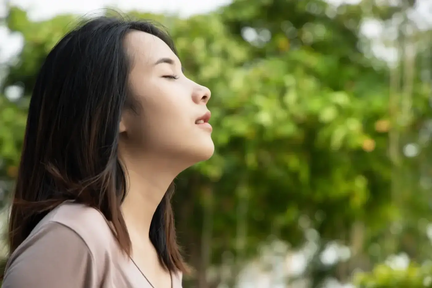 A young asian woman practicing Box Breathing with her eyes closed in a park.