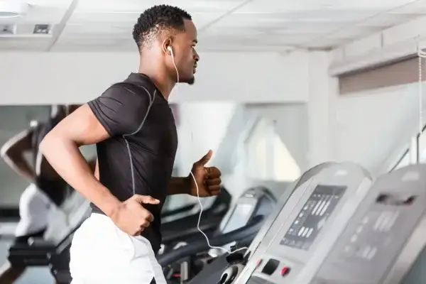 A man is engaged in transformative zone 2 cardiovascular exercise on a treadmill, harnessing its longevity benefits at the gym.