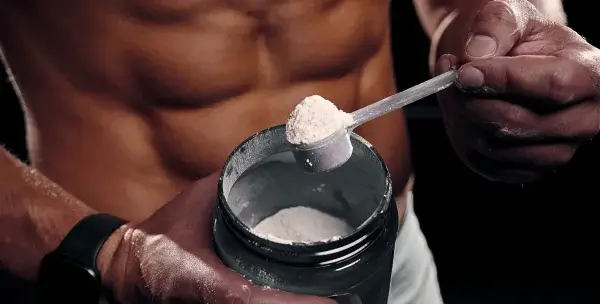 A man is holding a scoop of protein powder.