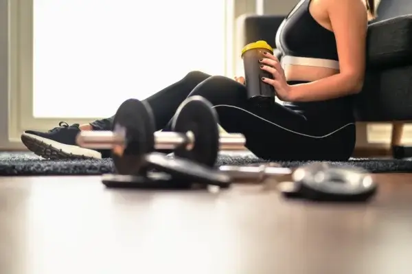 A woman practicing on the floor with a bottle of water and dumbbells, fostering longevity through fitness.