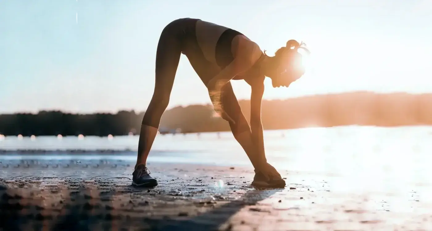 A woman stretching on the beach at sunset.