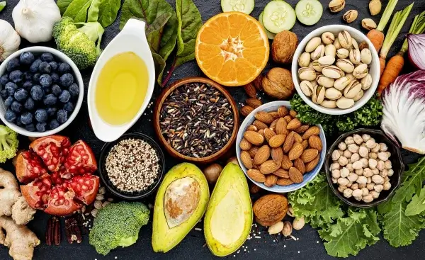 A variety of powerful, healthy foods including blueberries, nuts, vegetables, pomegranate, avocado, black rice, olive oil, and citrus fruits displayed on a dark surface sing a song of natural healing.
