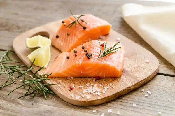 Two salmon fillets on a wooden cutting board.