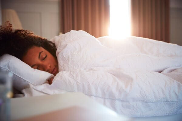 A woman enjoying a peaceful sleep in bed with a white blanket, promoting longevity.