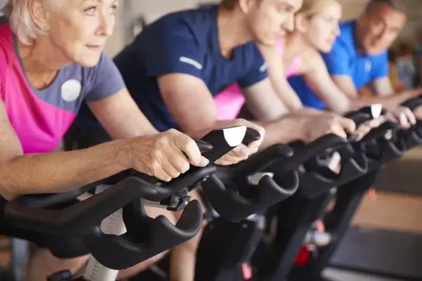A group of diverse adults, including an elderly woman, intensely focusing on building their VO2 max while using exercise bikes in a gym setting.