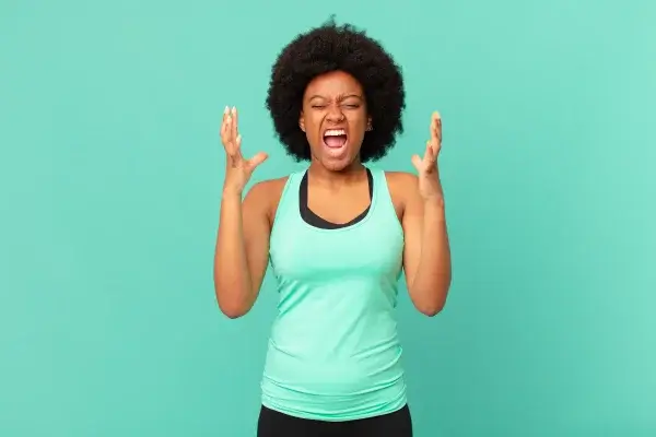 A person with an afro hairstyle is venting with their hands raised near their head against a green background, seemingly struggling with anger management.